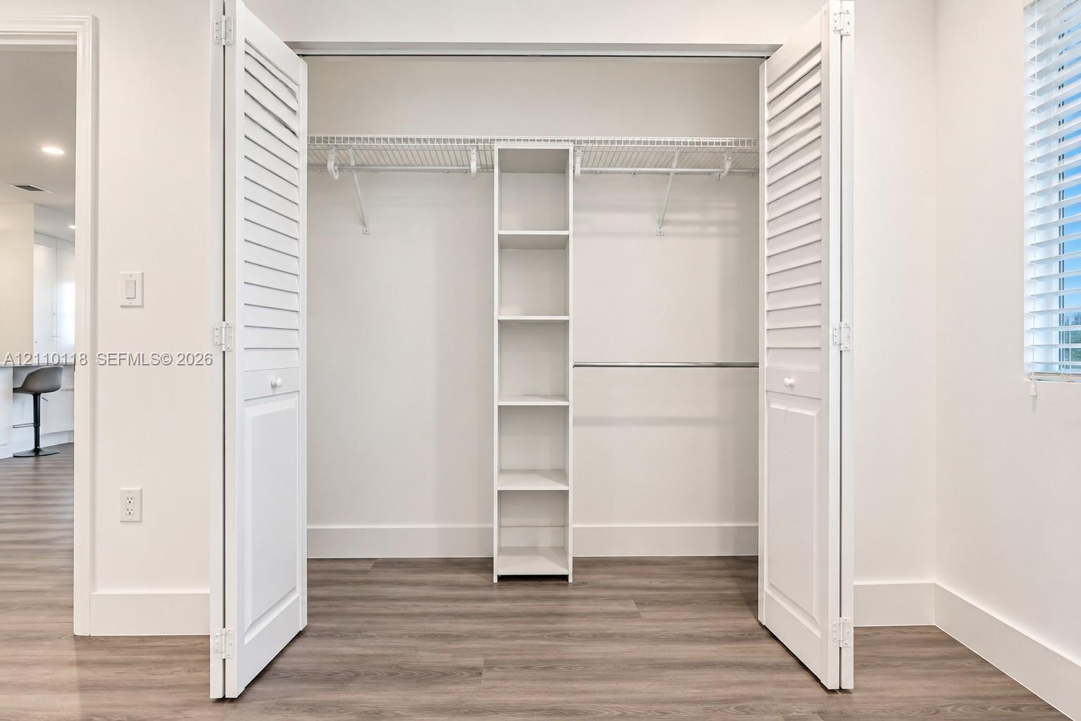 Closet featuring louvered bifold doors, built-in shelving unit, dual wire racks, and wood-finish flooring