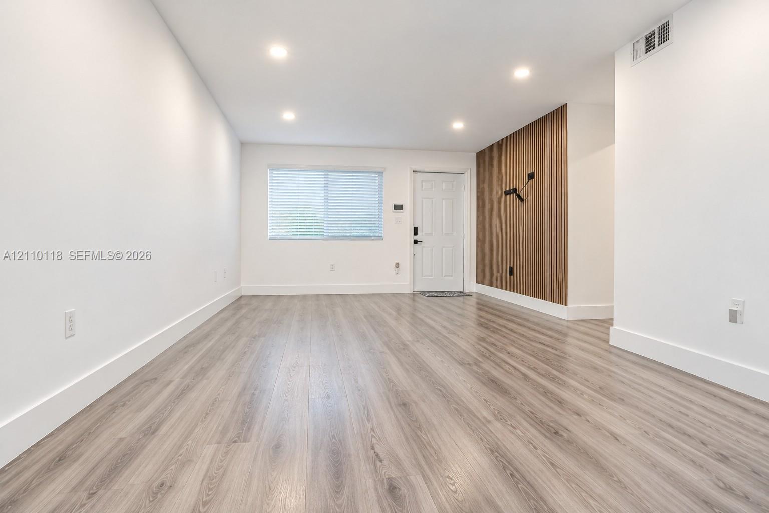 Interior space featuring wood-finish flooring, recessed lighting, and a vertical wood-slat accent wall with a wall-mounted light fixture