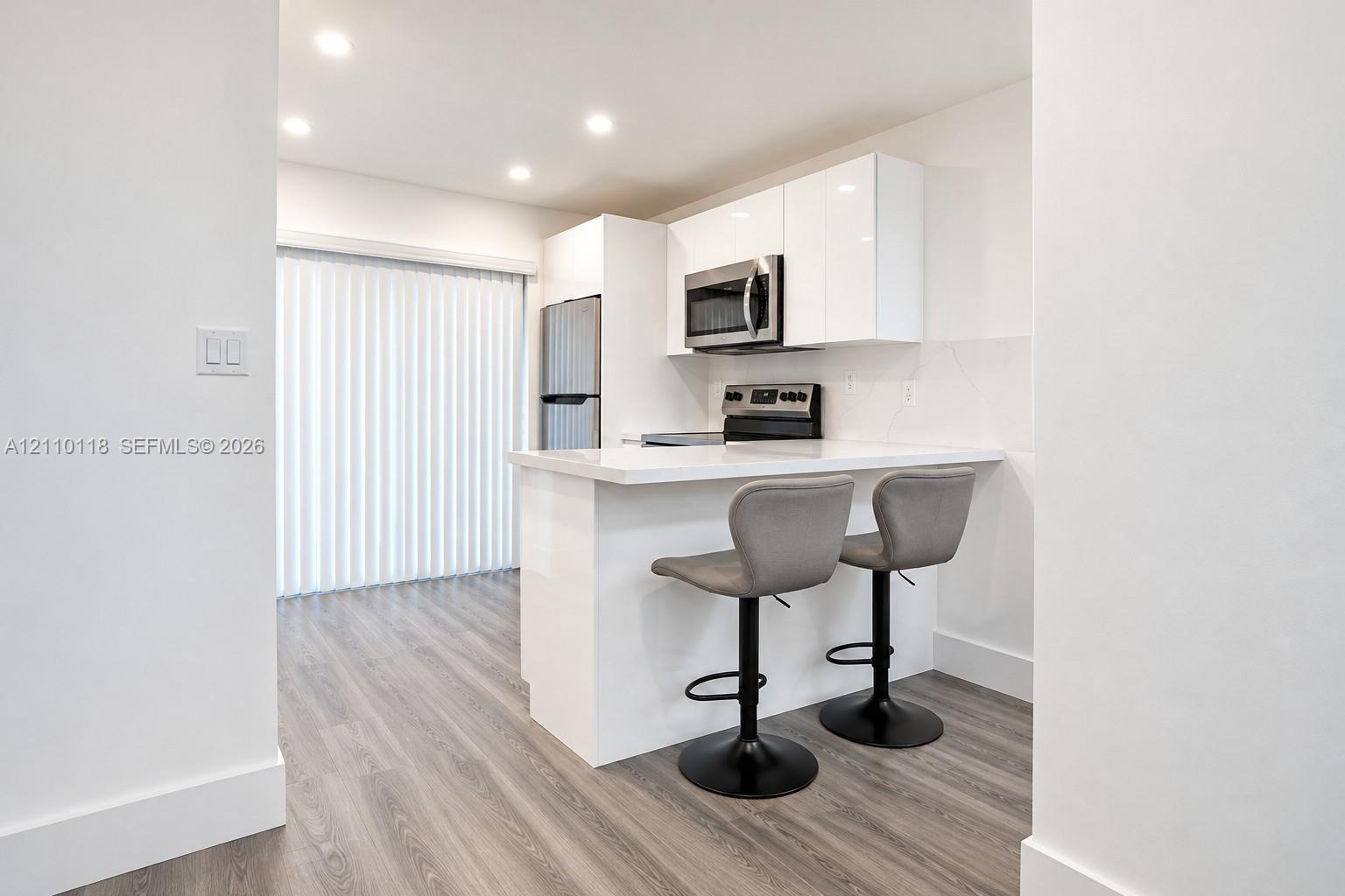 Kitchen featuring high-gloss white cabinetry, white stone-finish countertop with breakfast bar seating, stainless steel appliances, and wood-finish flooring