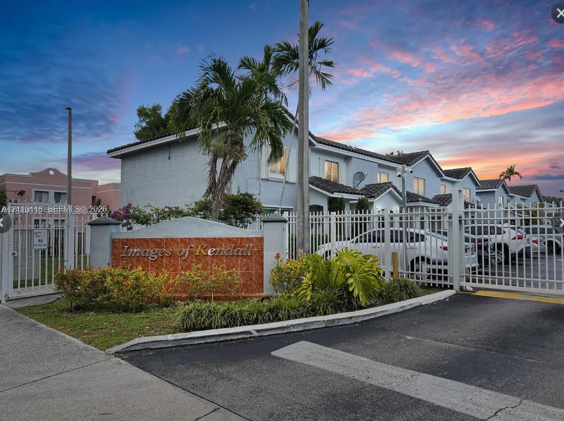 Gated residential entrance featuring custom stone-inlay signage, perimeter fencing, paved driveway, and mature landscaping