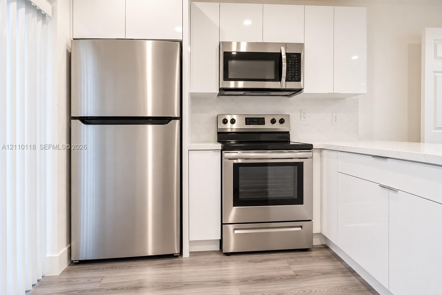 Kitchen featuring high-gloss white cabinetry, stainless steel appliances, solid surface countertops, and wood-finish flooring