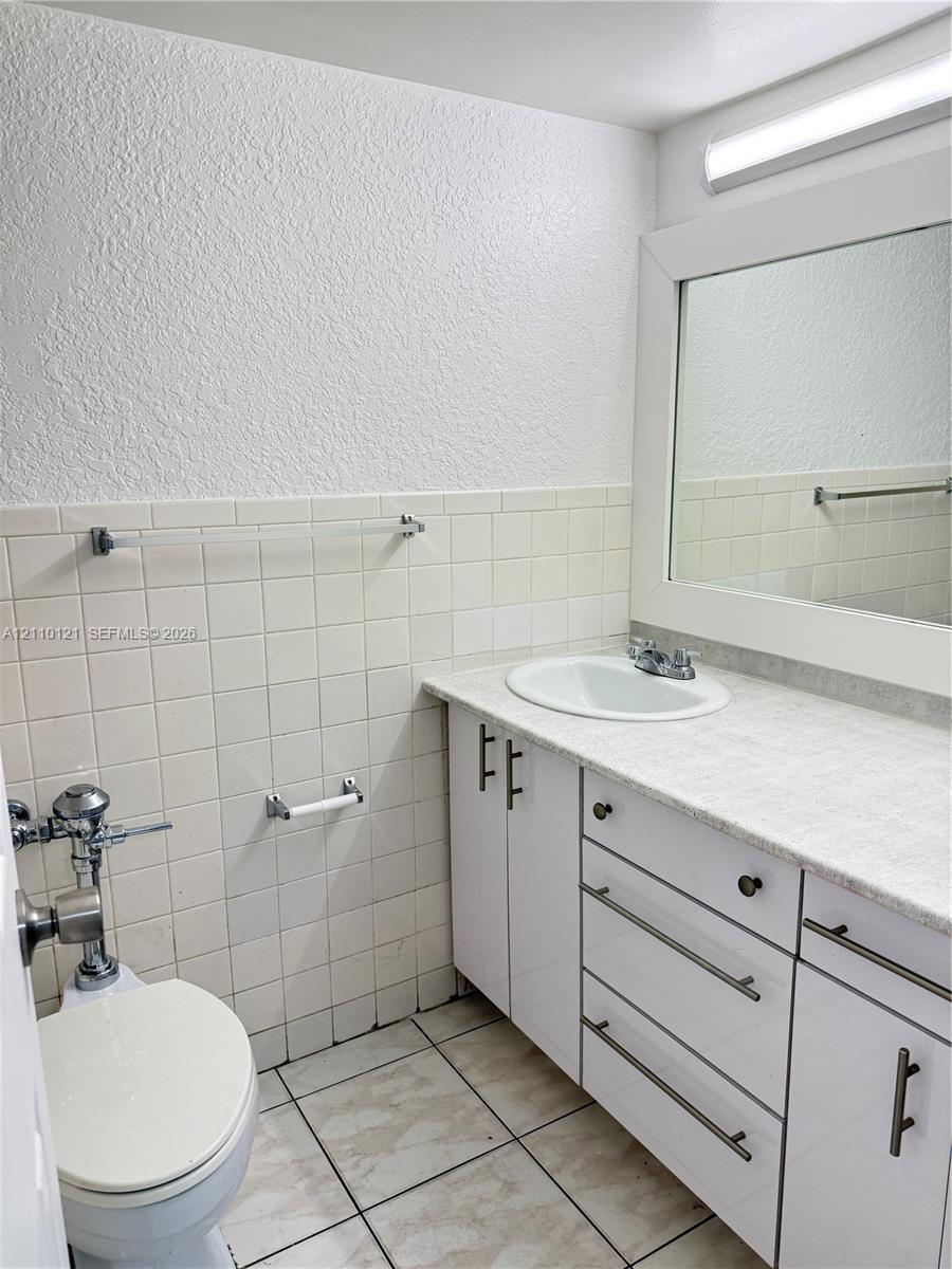 Bathroom featuring a white vanity cabinet with metallic hardware, integrated countertop with a recessed basin, framed wall mirror, and ceramic tile wall accents