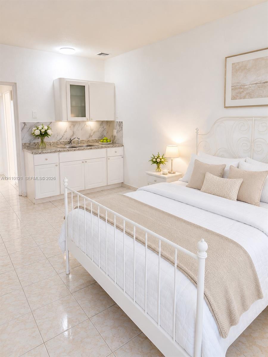 Built-in kitchenette featuring white cabinetry, stone-finish countertops, tile backsplash, and an integrated double-basin sink, complemented by light-toned tile flooring