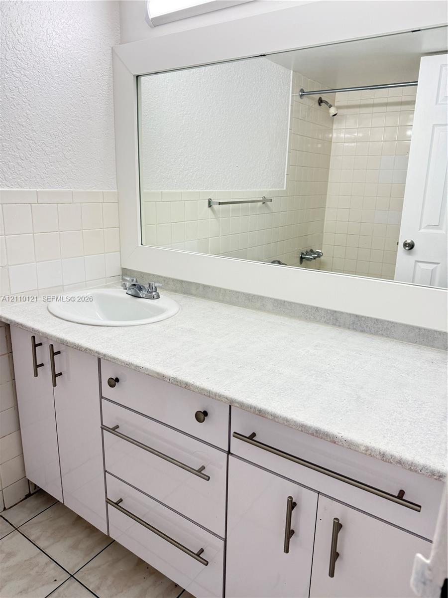 Bathroom vanity featuring white cabinetry, stone-finish countertop, integrated oval sink, modern bar-style hardware, and full-width wall mirror