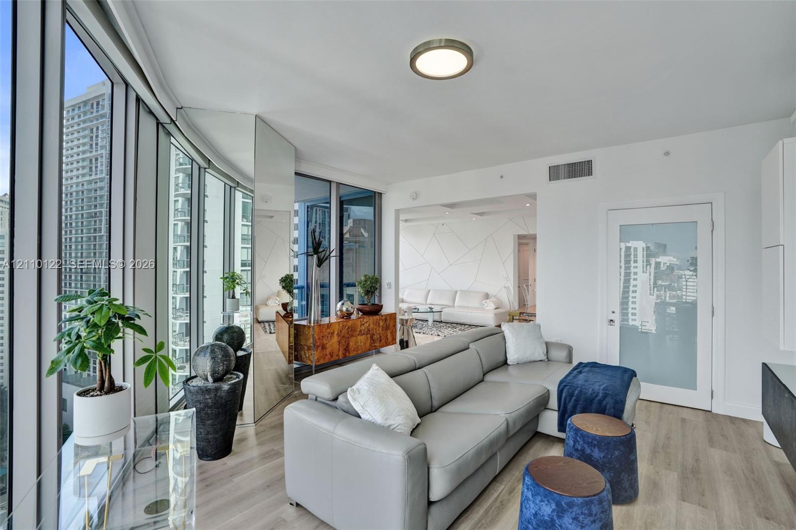 Floor-to-ceiling windows, wood-finish flooring, full-height mirrored wall panel, and a frosted glass-paneled interior door