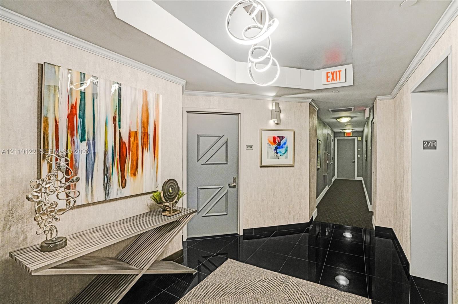 Foyer featuring black tiled flooring, a recessed tray ceiling with sculptural pendant lighting, and textured wall coverings