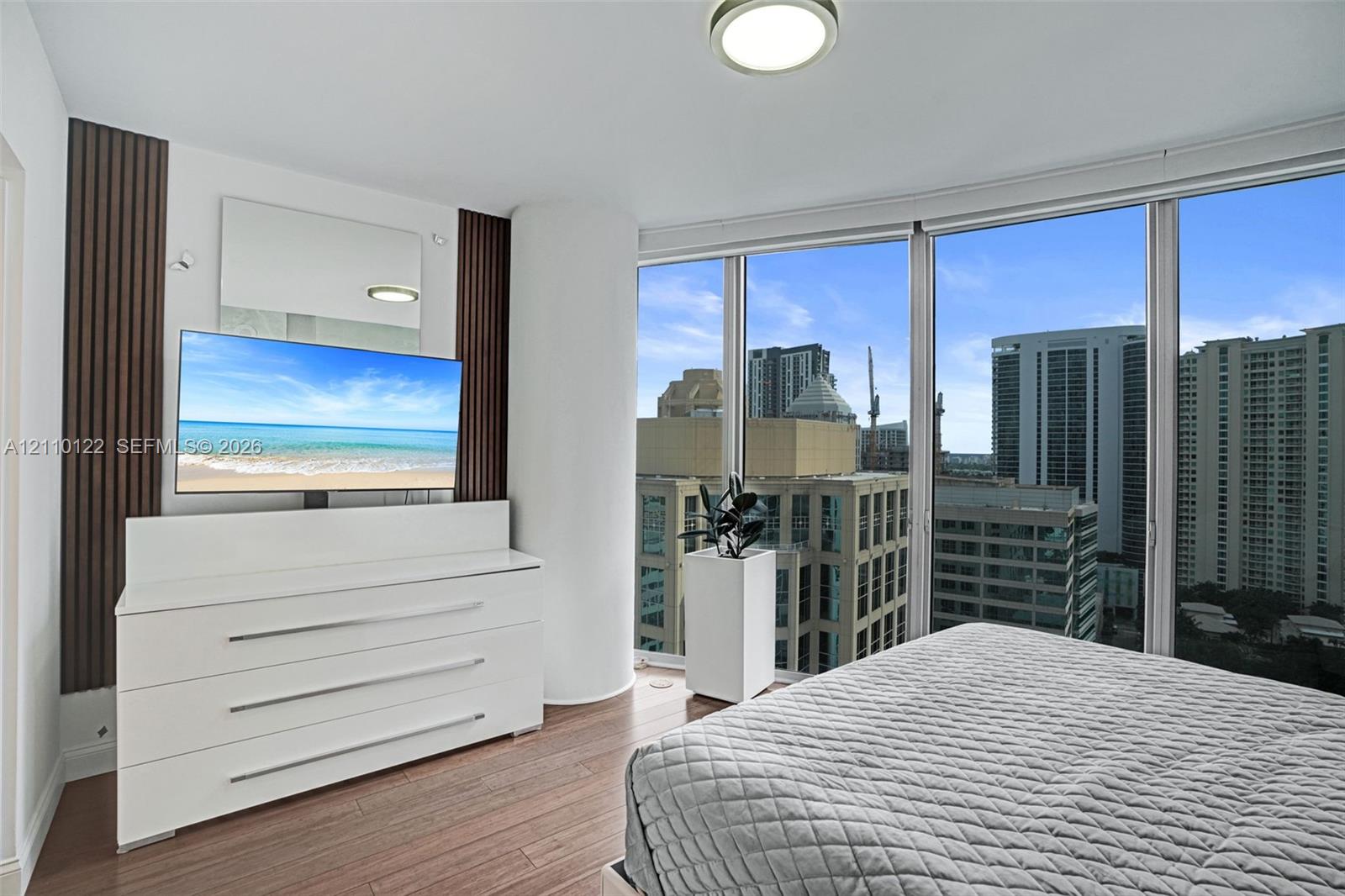 Floor-to-ceiling windows featuring urban scenery, wood-finish flooring, and decorative vertical wall paneling