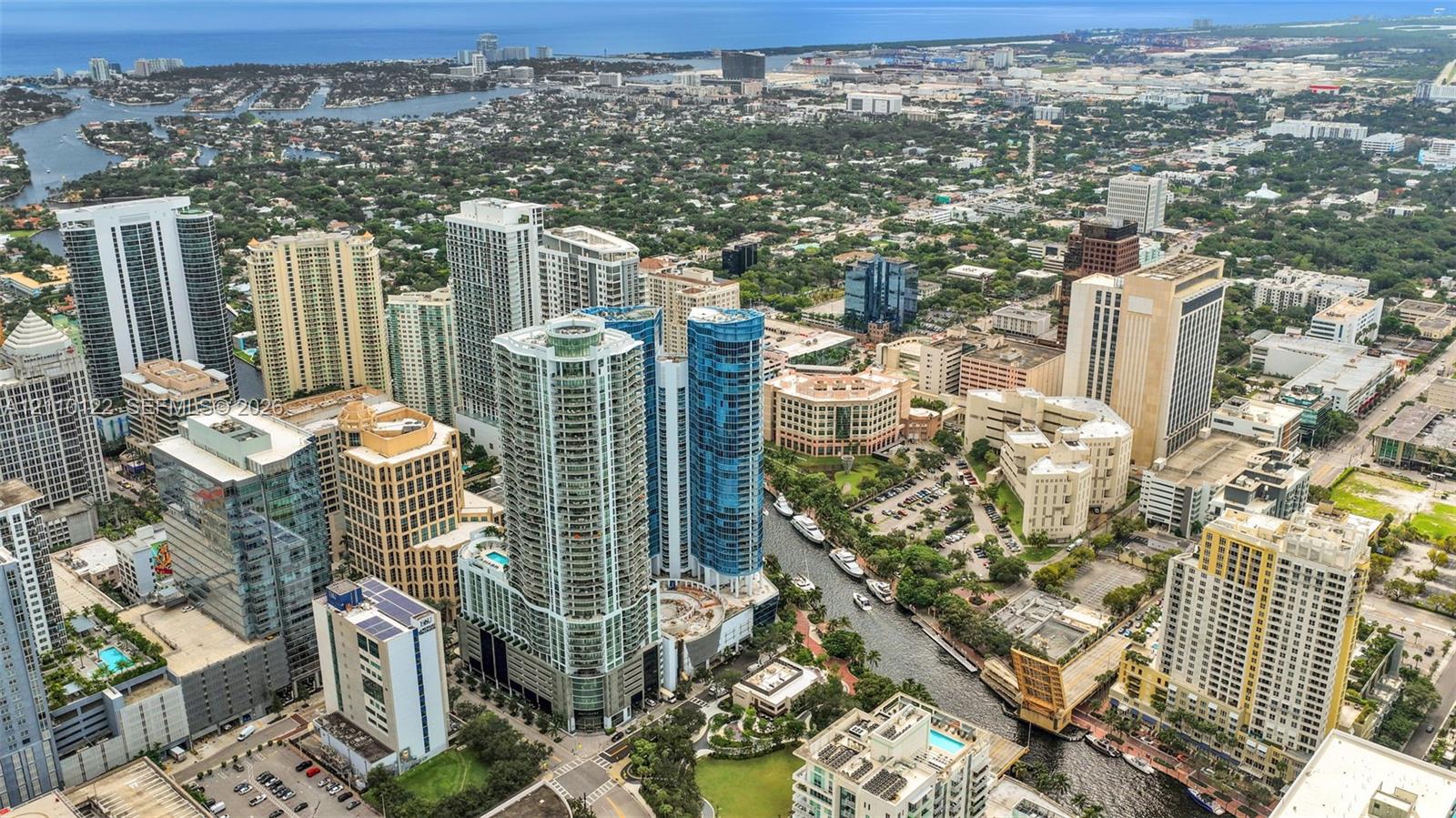 Aerial perspective of high-rise structures featuring glass curtain walls, balconies, integrated parking facilities, and immediate proximity to urban waterways