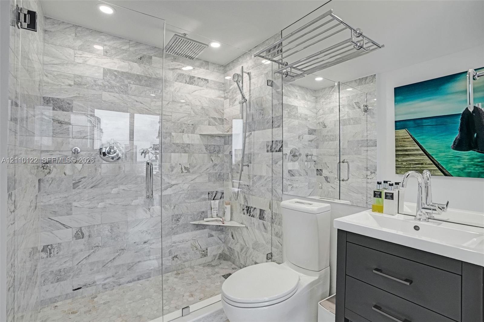 Walk-in shower with floor-to-ceiling stone tile, glass enclosure, rainfall shower head, handheld sprayer, and recessed shelving