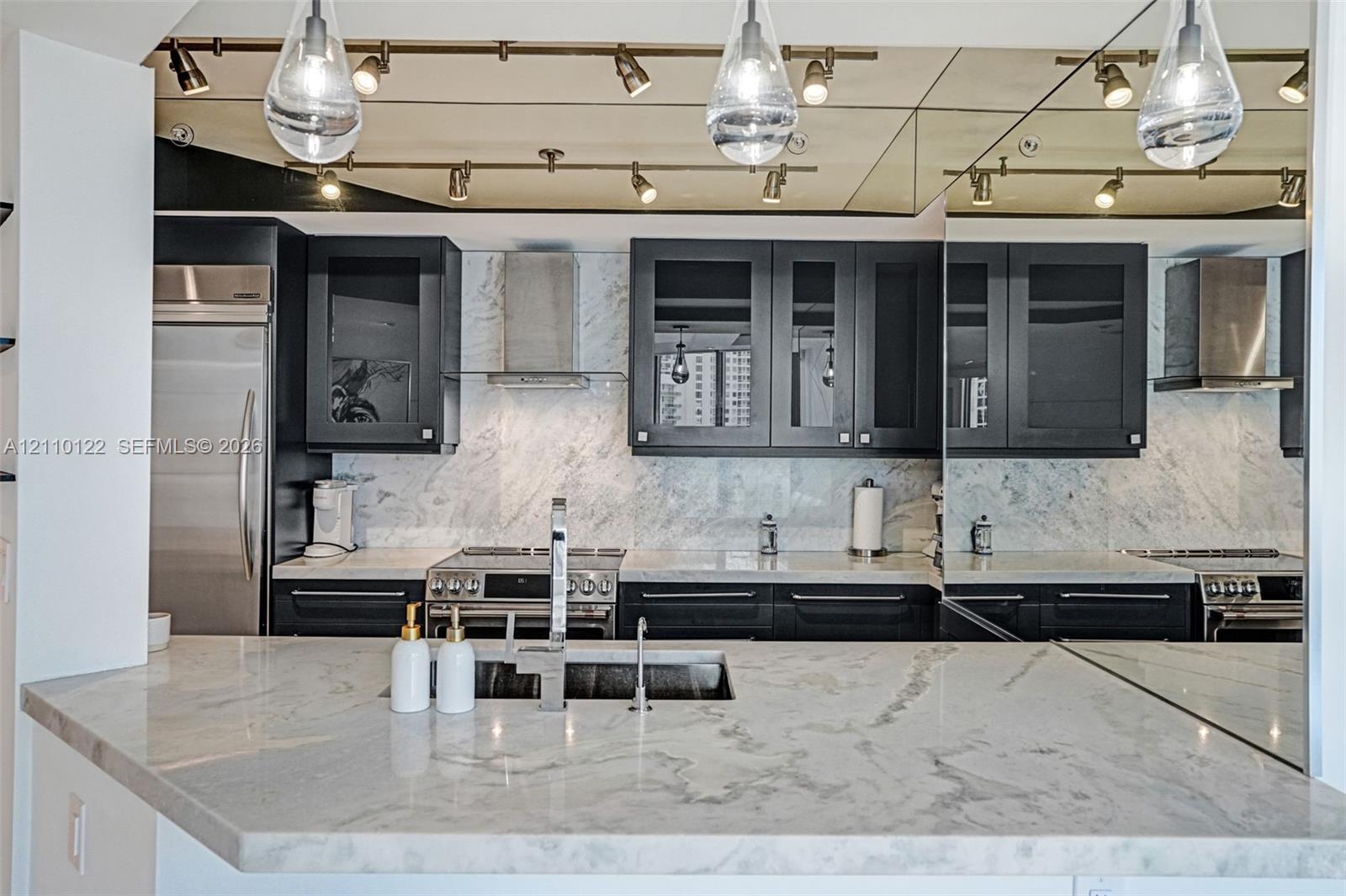 Kitchen featuring dark cabinetry, stone countertops, stone tile backsplash, stainless steel appliances, and mounted track lighting