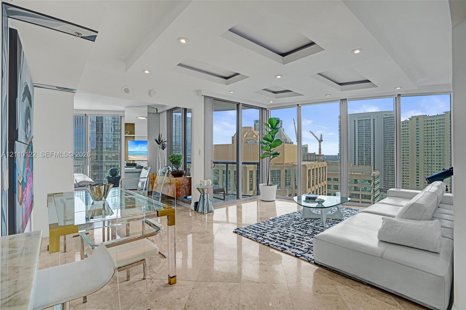 Living space featuring floor-to-ceiling windows, polished stone flooring, recessed tray ceiling detailing, and integrated lighting Living space featuring floor-to-ceiling windows, polished stone flooring, recessed tray ceiling detailing, and integrated lighting