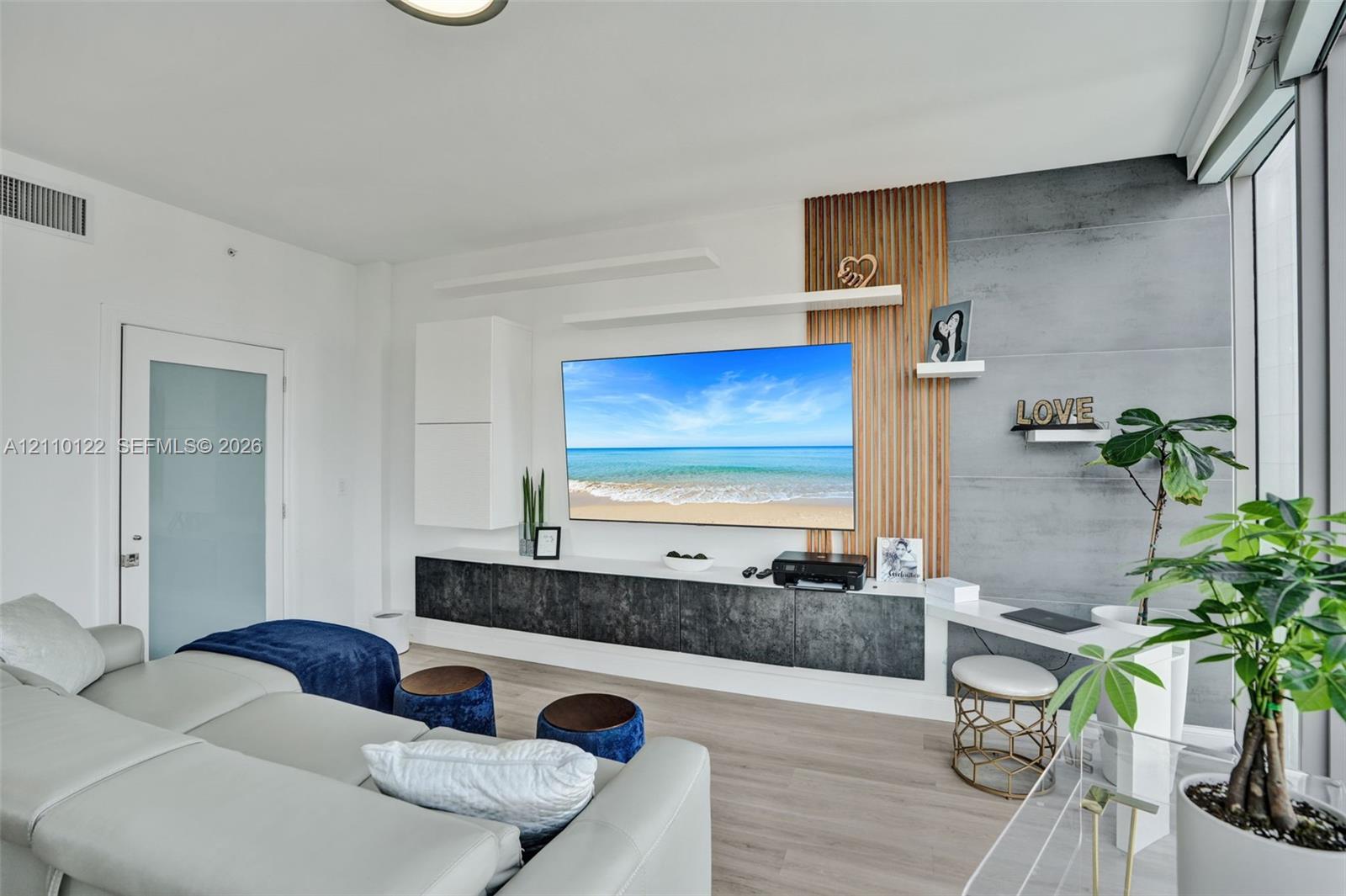 Custom built-in media console featuring vertical wood slat paneling, dark textured cabinetry, concrete-finish wall detail, floating display shelves, and integrated desk workspace