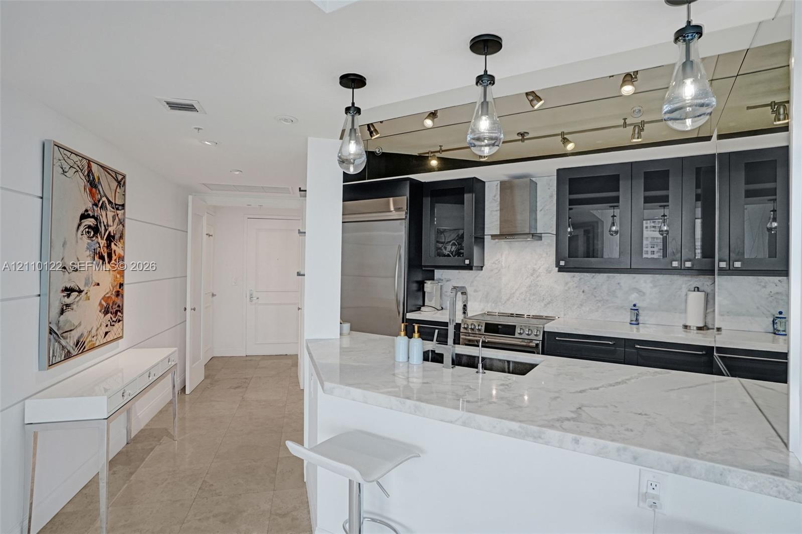 Kitchen featuring stone countertops, dark-finished cabinetry with glass-panel inserts, stainless steel appliances, and teardrop pendant lighting