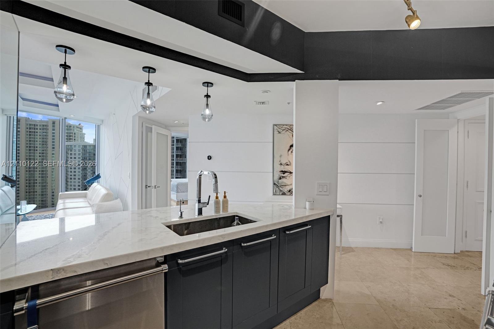 Kitchen featuring stone countertops, dark cabinetry, stainless steel undermount sink, pendant lighting, and polished stone flooring