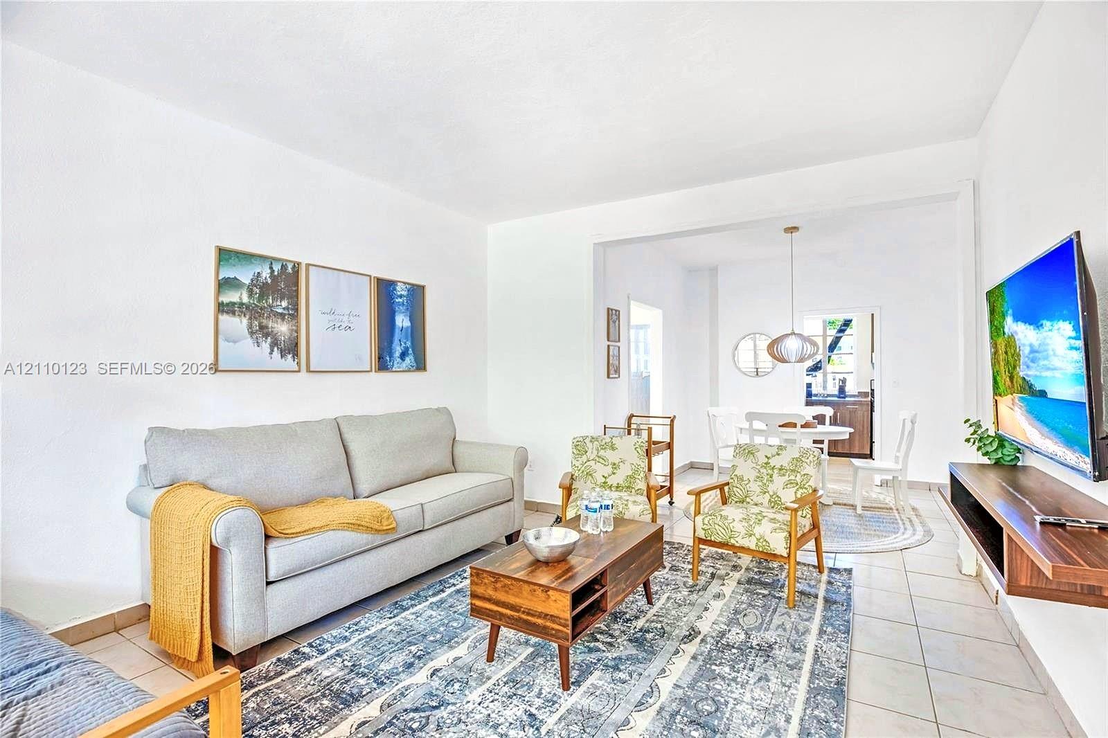 Open-concept interior featuring neutral wall finishes, ceramic tile flooring, a wall-mounted wooden media shelf, and a contemporary pendant light fixture