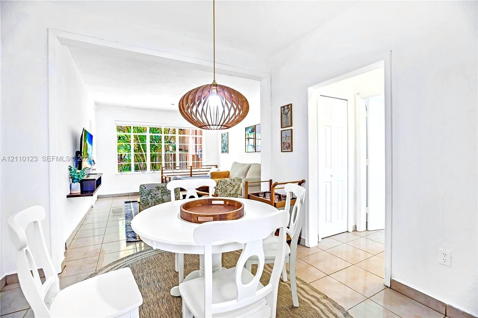 Dining area featuring large-format ceramic tile flooring, a geometric lattice-style pendant light fixture, and a floating wall-mounted shelf