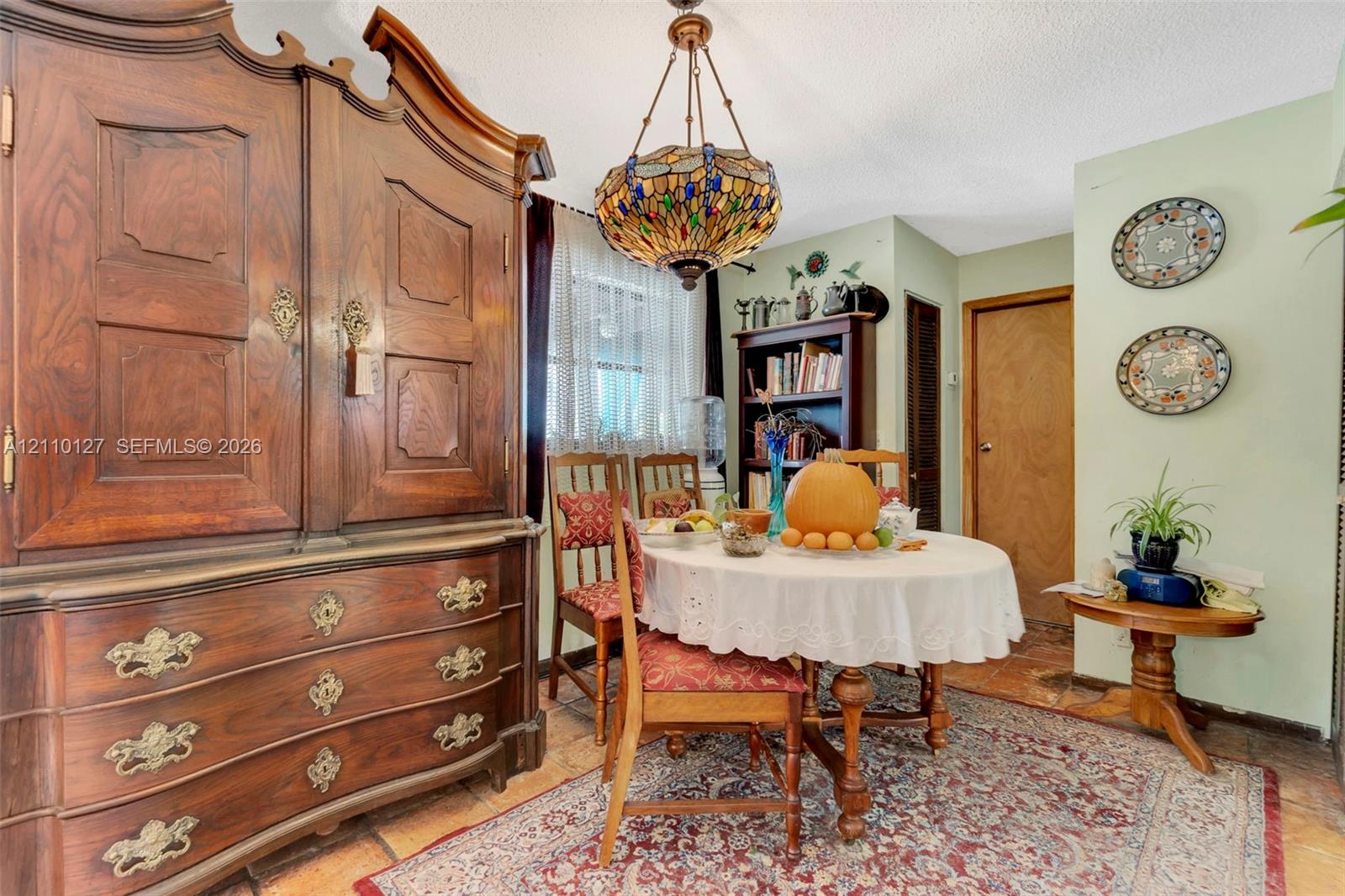 Stained-glass chandelier with intricate metal detailing, wood-finish tile flooring, and built-in wood shelving unit