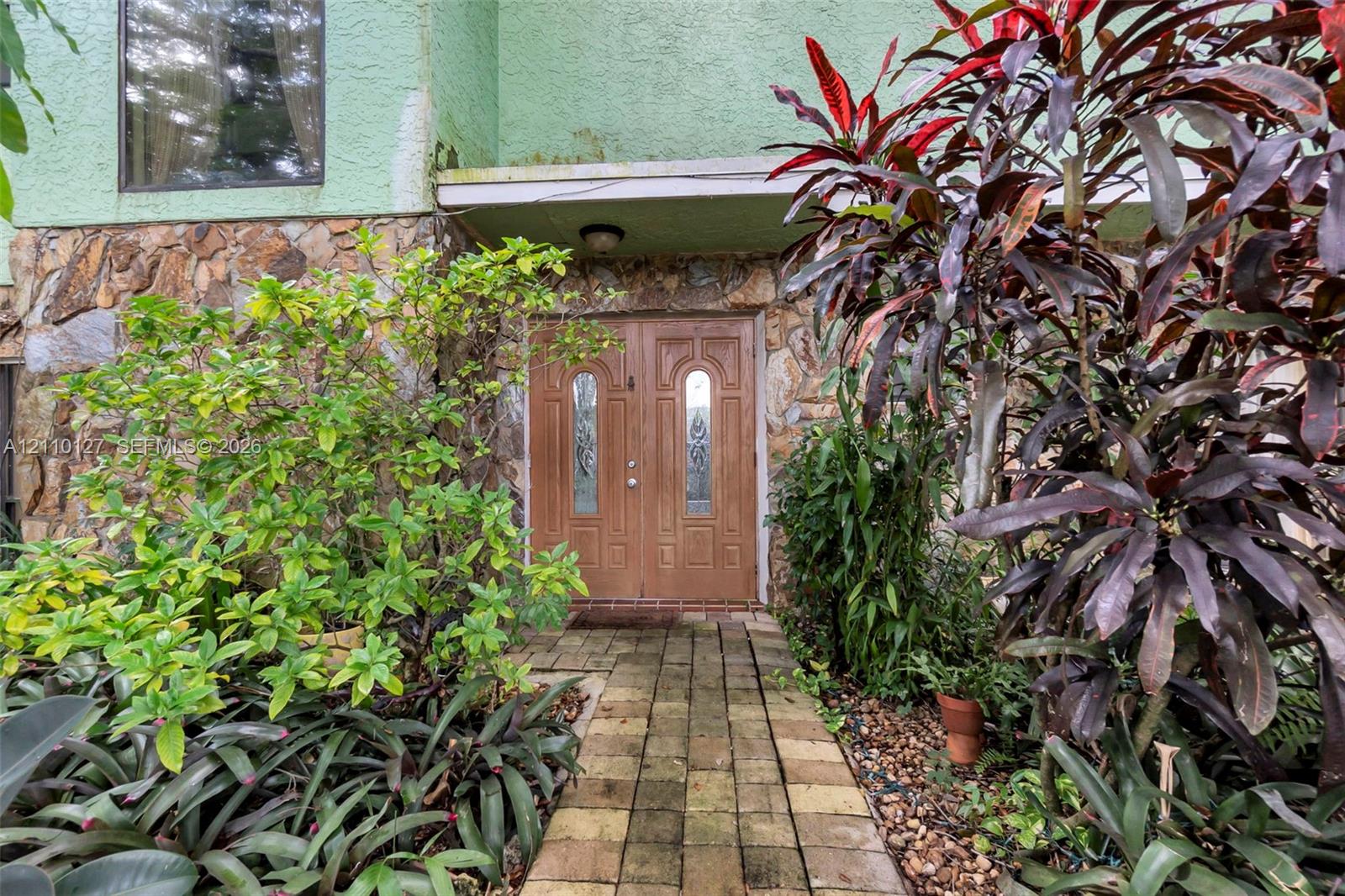 Exterior entrance featuring double doors with decorative glass inserts, natural stone masonry facade, stucco detailing, and a brick paver walkway