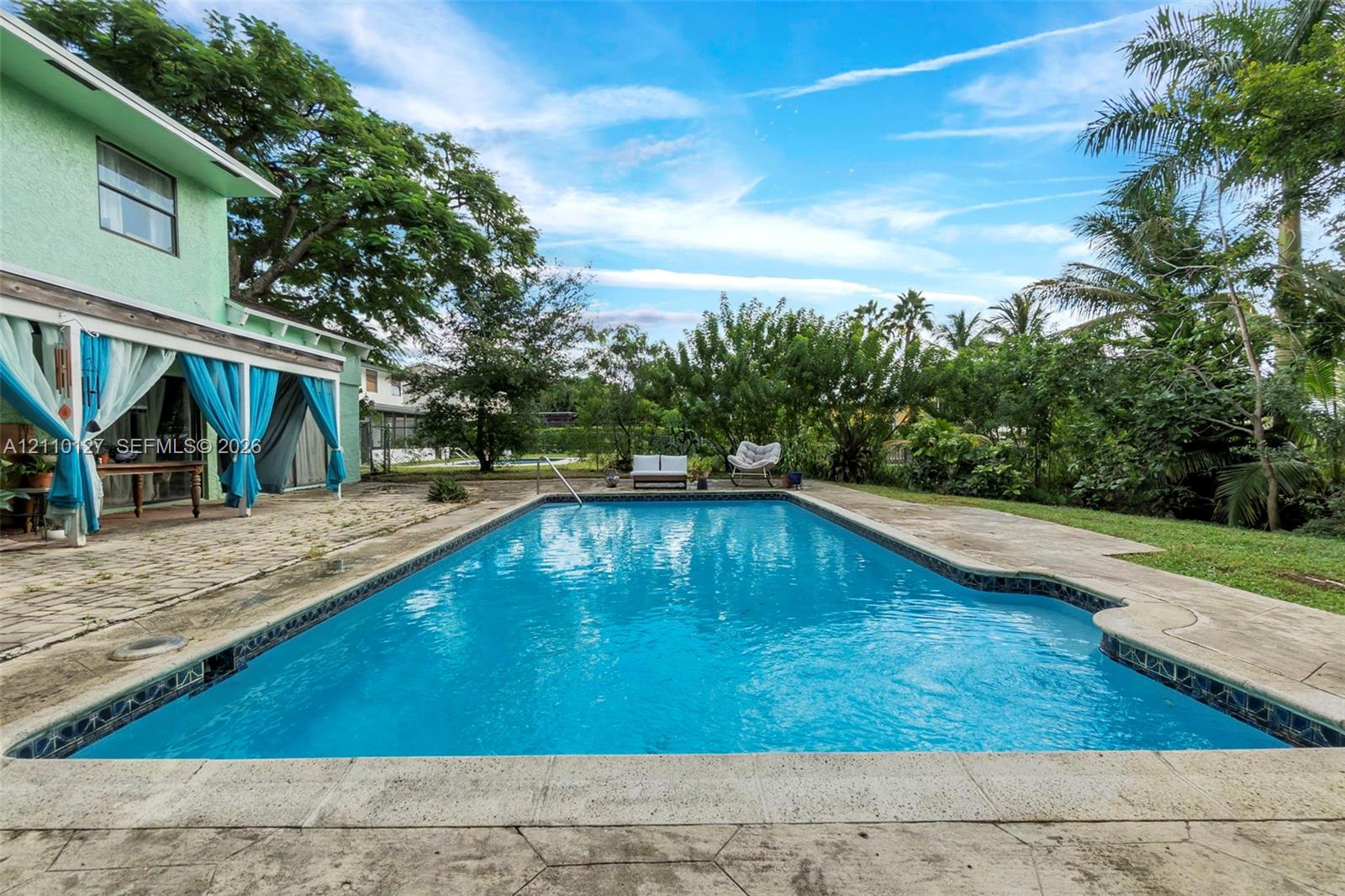 In-ground swimming pool featuring a concrete deck, covered patio, and established landscaping