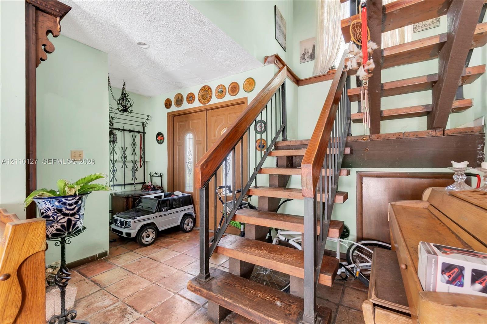 Foyer entry featuring dual wood doors with glass inserts, terra cotta tile flooring, and an open-riser staircase with wood treads and metal balusters