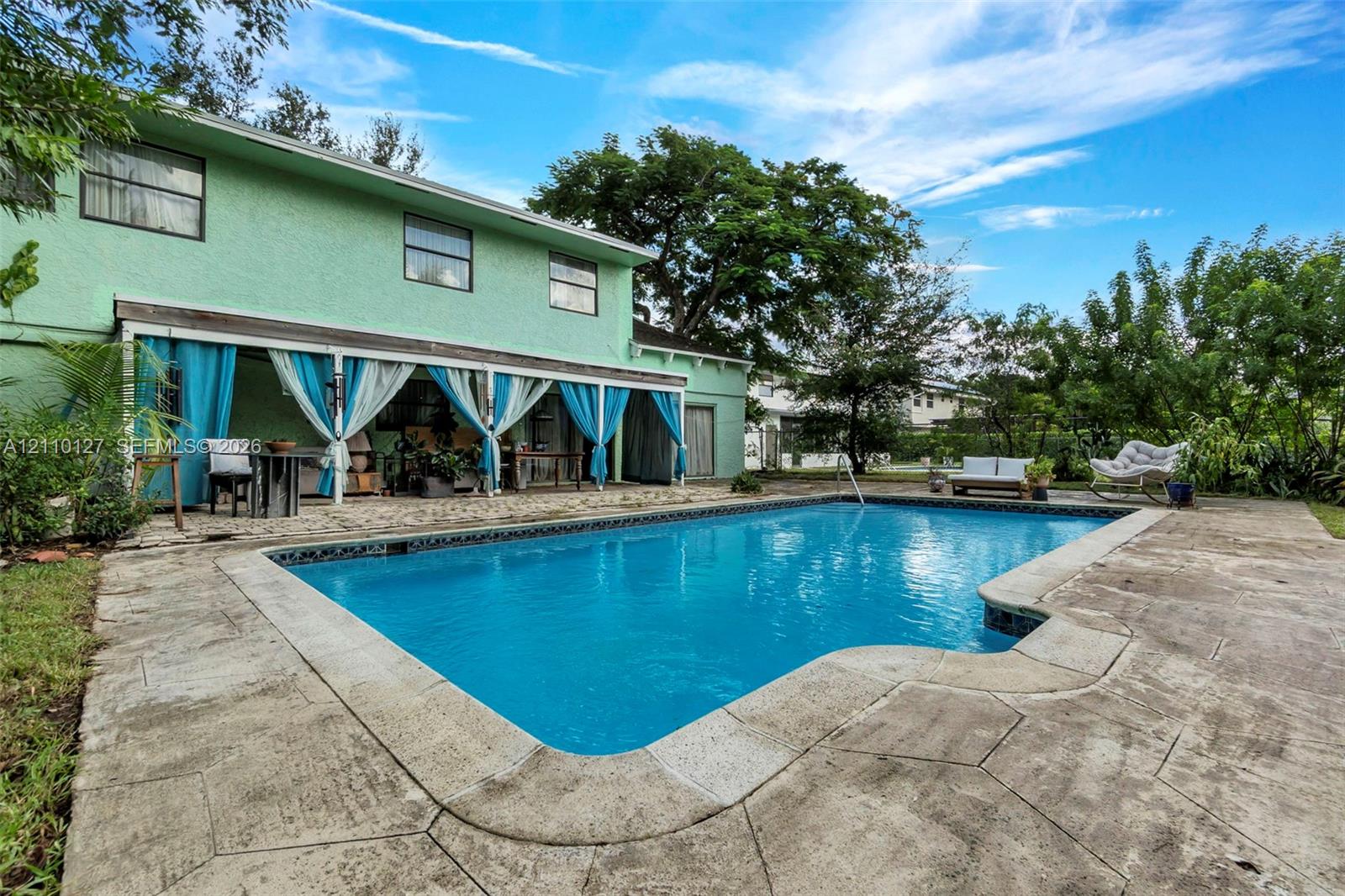 In-ground swimming pool featuring a concrete deck and a covered patio area with a support structure
