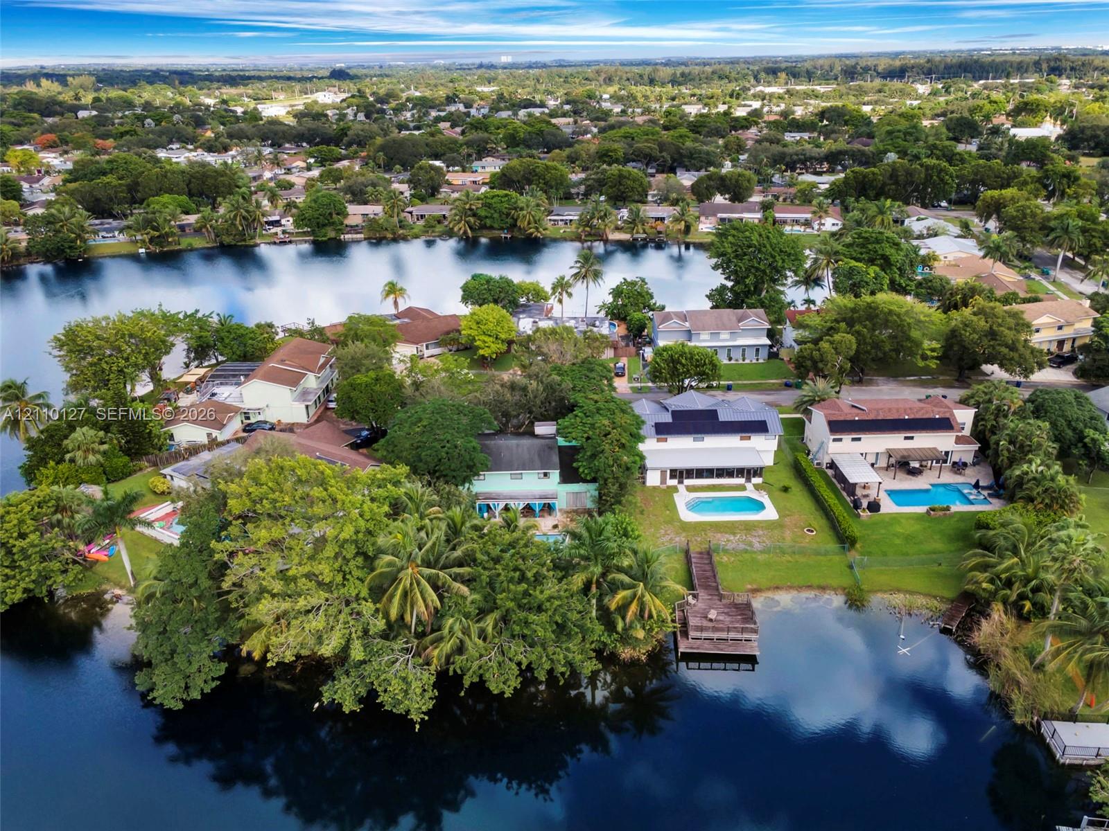 Waterfront residential setting featuring a private dock, swimming pools, mature landscaping, and solar panel arrays Waterfront residential setting featuring a private dock, swimming pools, mature landscaping, and solar panel arrays