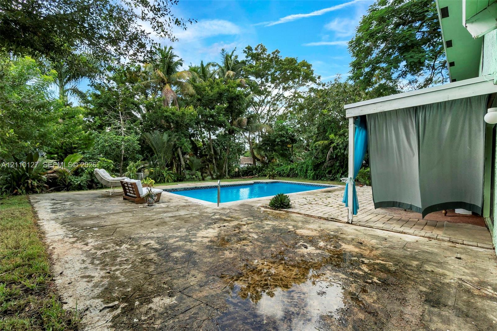 In-ground swimming pool featuring a concrete patio, covered porch area, and mature landscaping