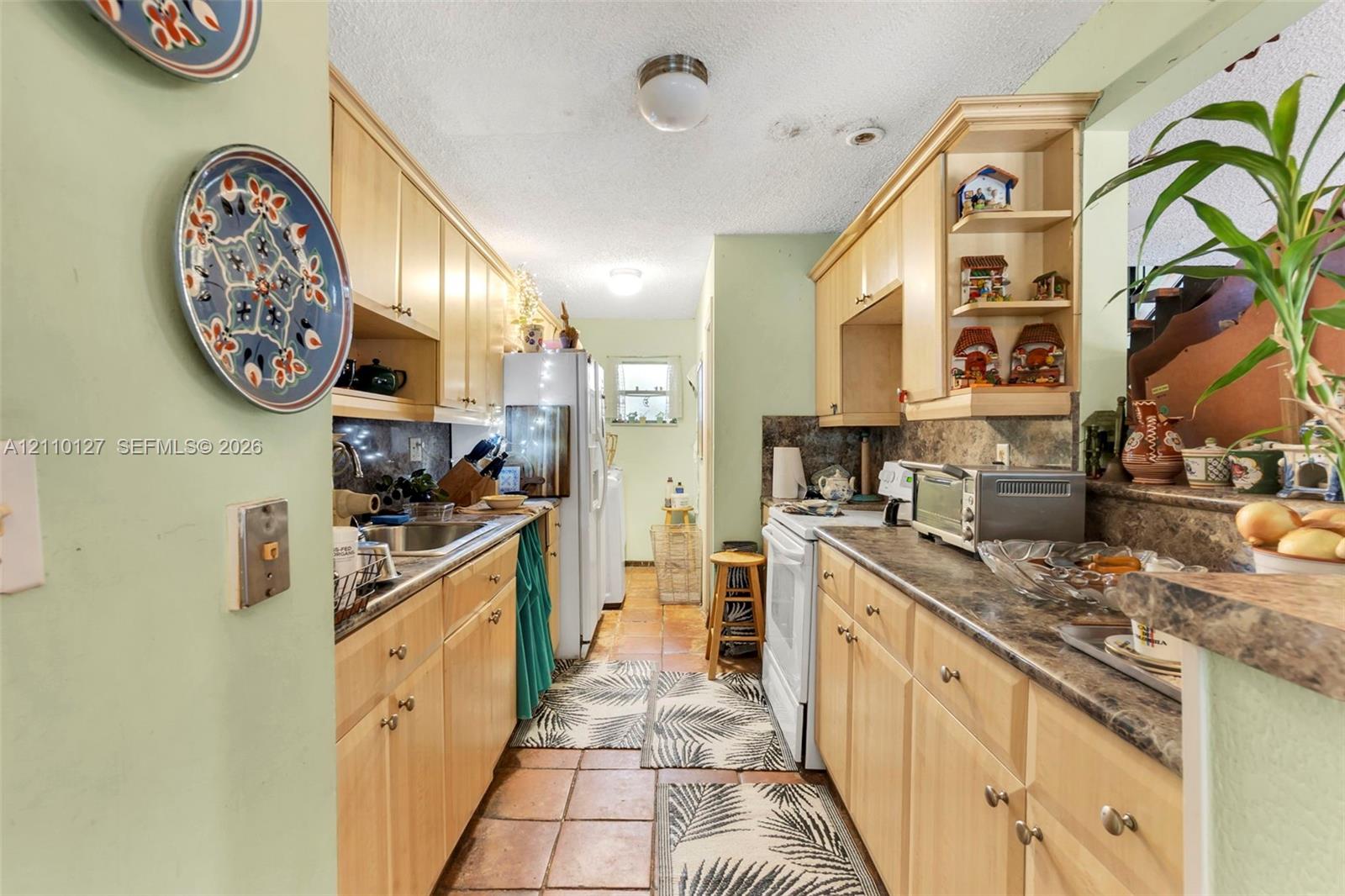 Galley-style kitchen featuring light-tone wood cabinetry, built-in open shelving, laminate countertops, and ceramic tile flooring