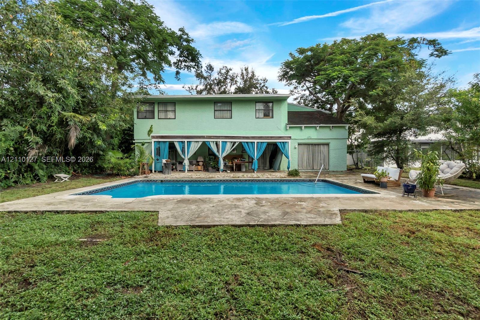 Two-story residence featuring a covered patio, swimming pool with concrete decking, and mature trees on the property grounds