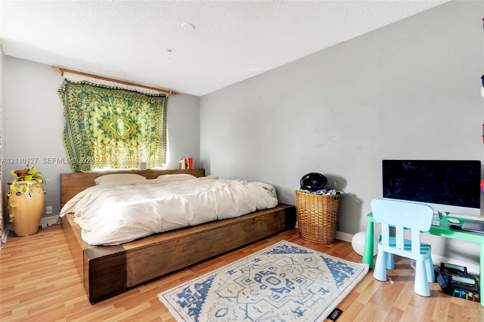 Bedroom interior featuring neutral wall paint, wood-finish flooring, and a window with a mounted curtain rod