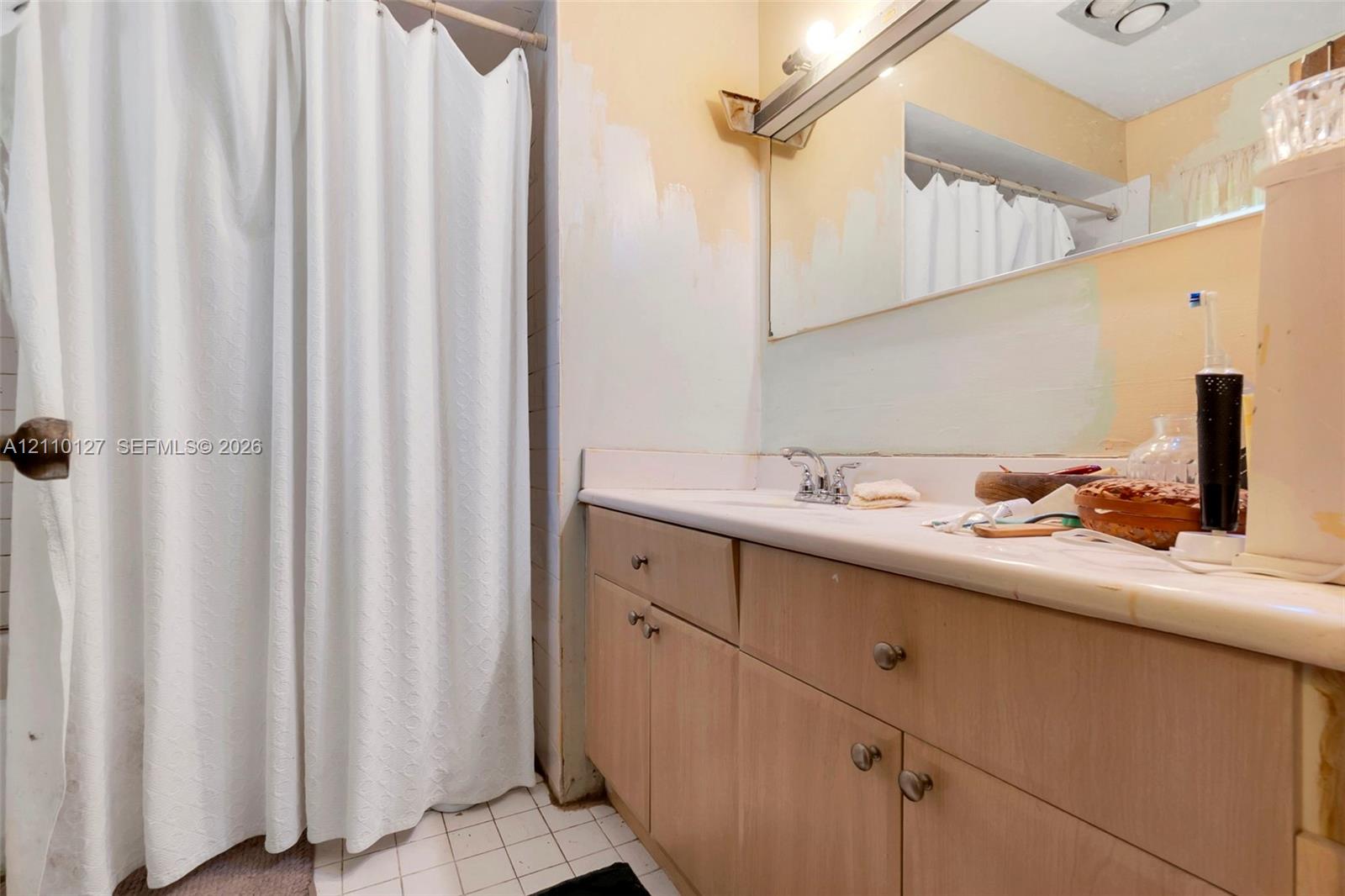 Bathroom featuring a vanity with light-tone wood-finish cabinetry, a solid-surface countertop with an integrated sink, a large wall-mounted mirror, and a shower area with a curtain rod