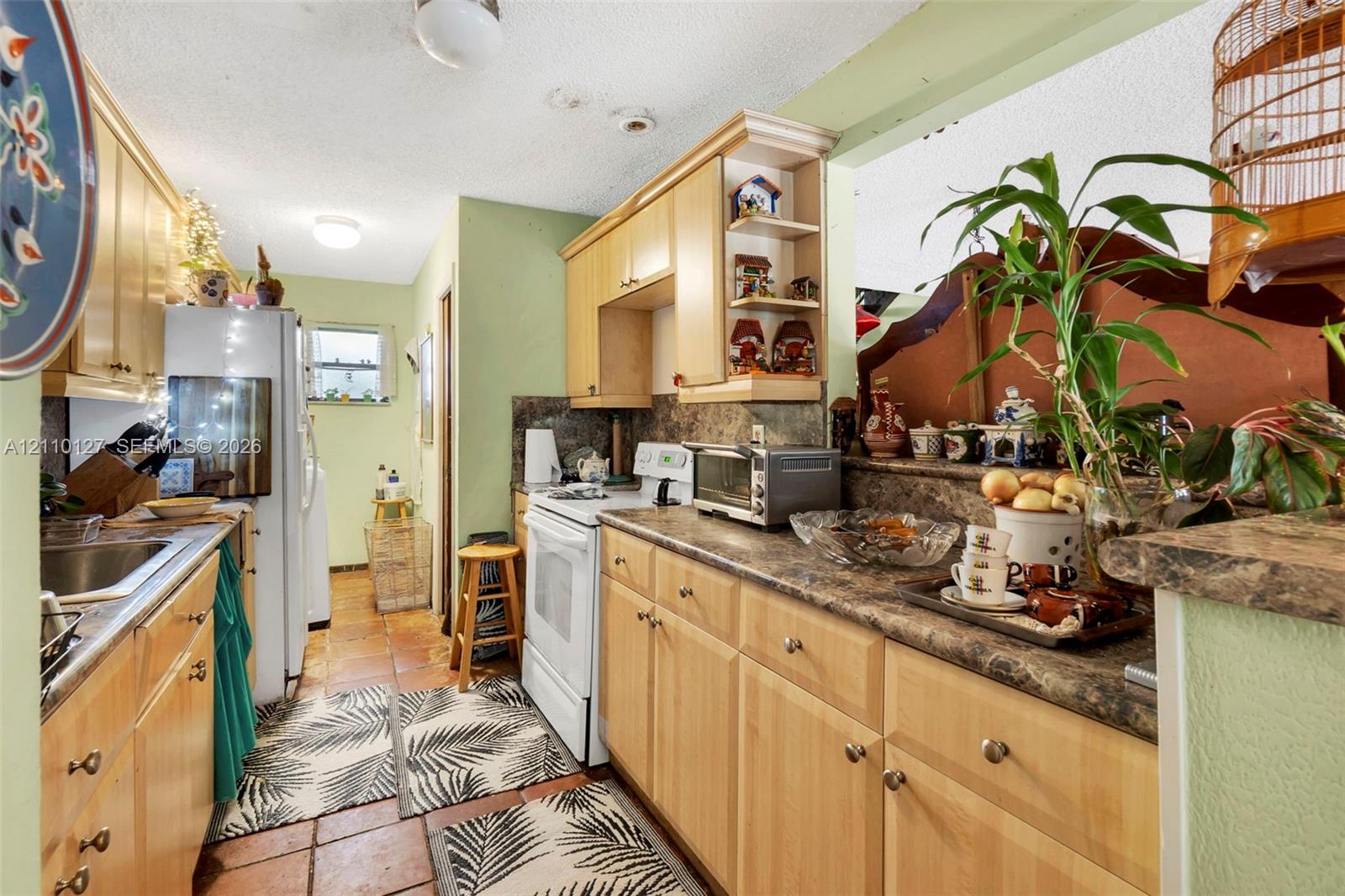 Kitchen featuring light-finish wood cabinetry, laminate countertops with a stone-pattern finish, ceramic tile flooring, and integrated open corner shelving