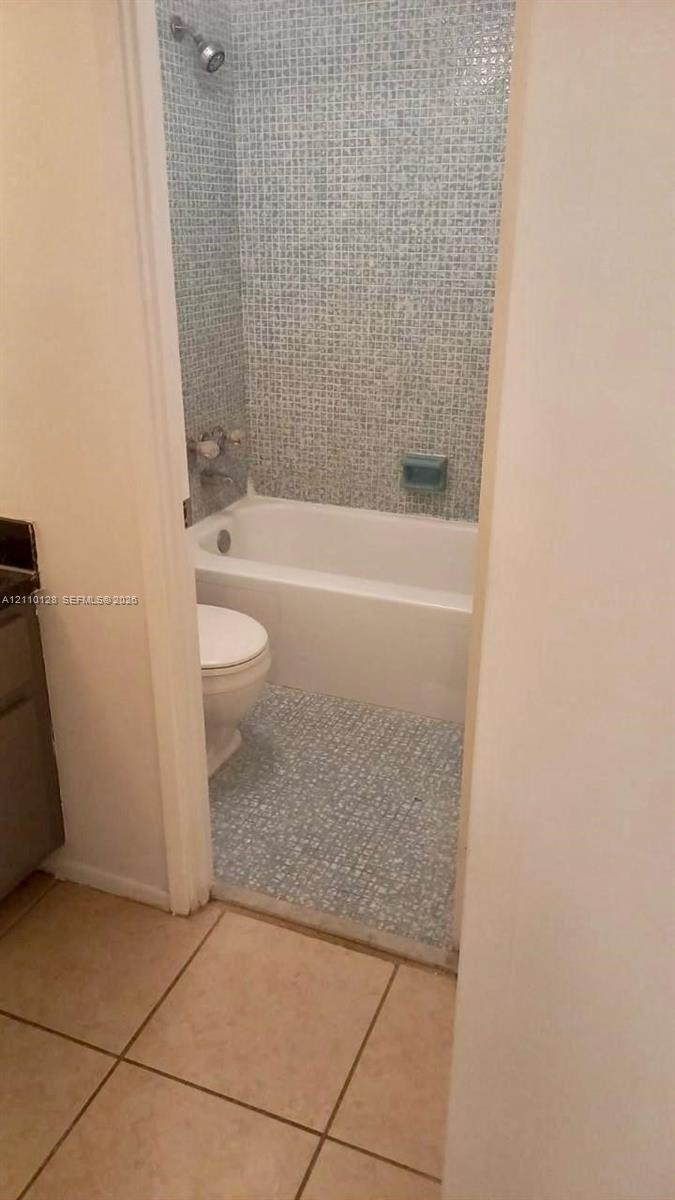 Bathroom featuring blue mosaic wall tile, a white porcelain soaking tub, a built-in soap niche, and light-toned floor tiling