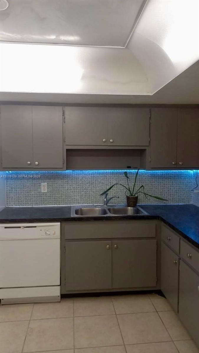 Kitchen featuring painted cabinetry, dark solid-surface countertops, mosaic tile backsplash, integrated under-cabinet lighting, and a stainless steel double-basin sink