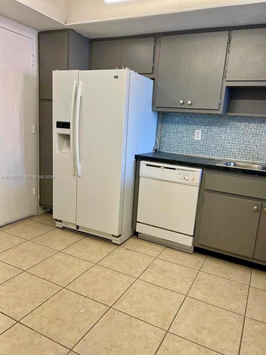 Kitchen featuring grey cabinetry, dark solid-surface countertops, decorative mosaic tile backsplash, ceramic tile flooring, and integrated appliances