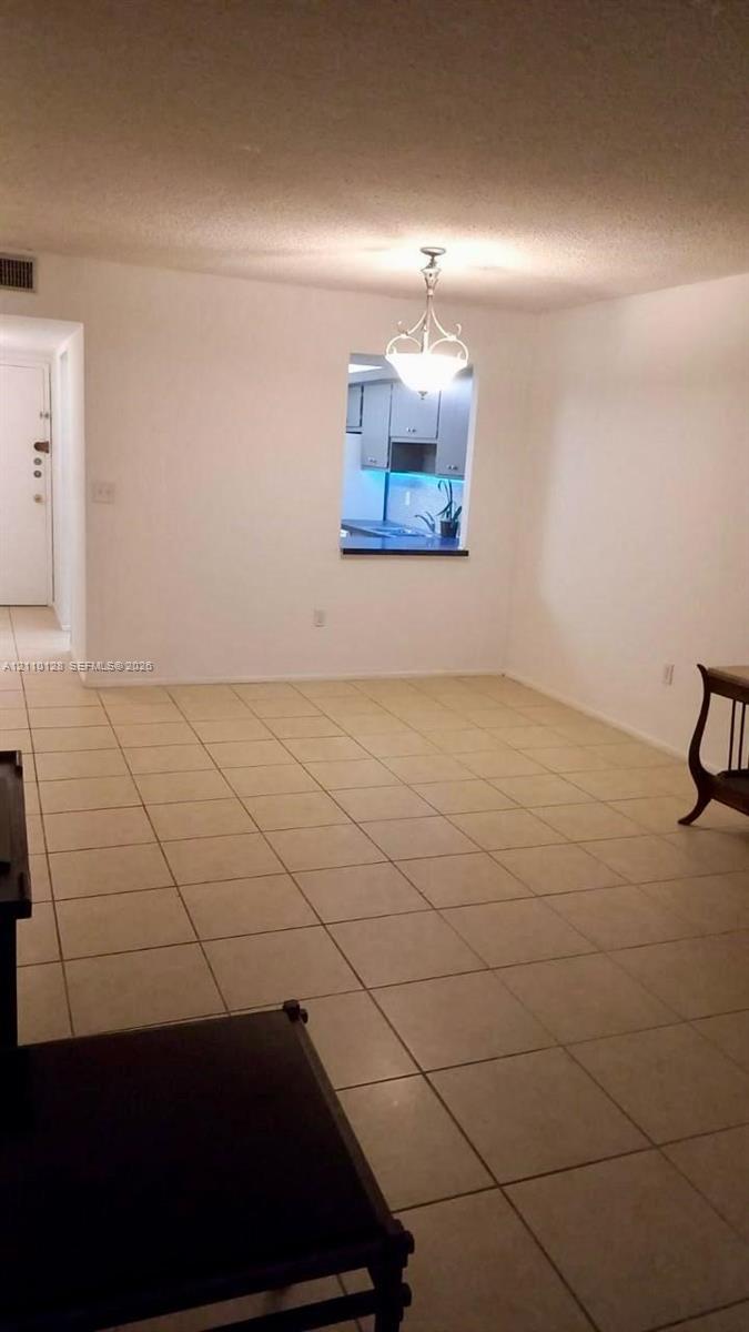 Open-concept space featuring neutral tile flooring, a decorative chandelier, and a kitchen pass-through window with a countertop ledge