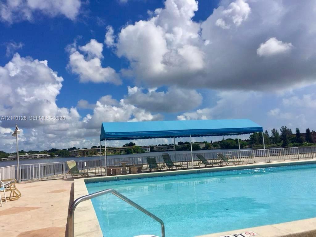 In-ground swimming pool featuring a metal safety railing, paved decking, and a blue fabric canopy structure