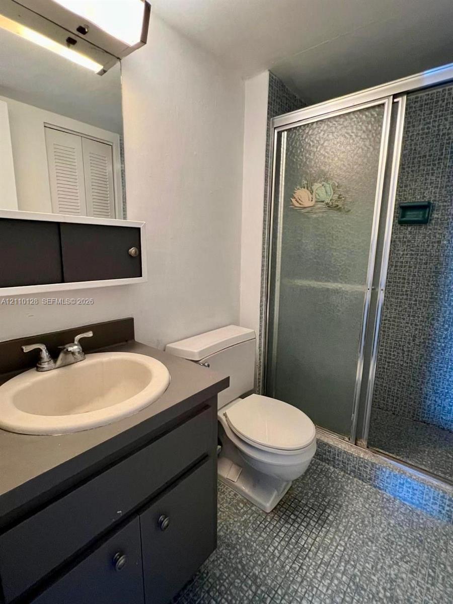 Bathroom featuring a dark-finish vanity with a drop-in sink, wall-mounted medicine cabinet, modern linear vanity light, and a walk-in shower with textured glass doors and tiled surround