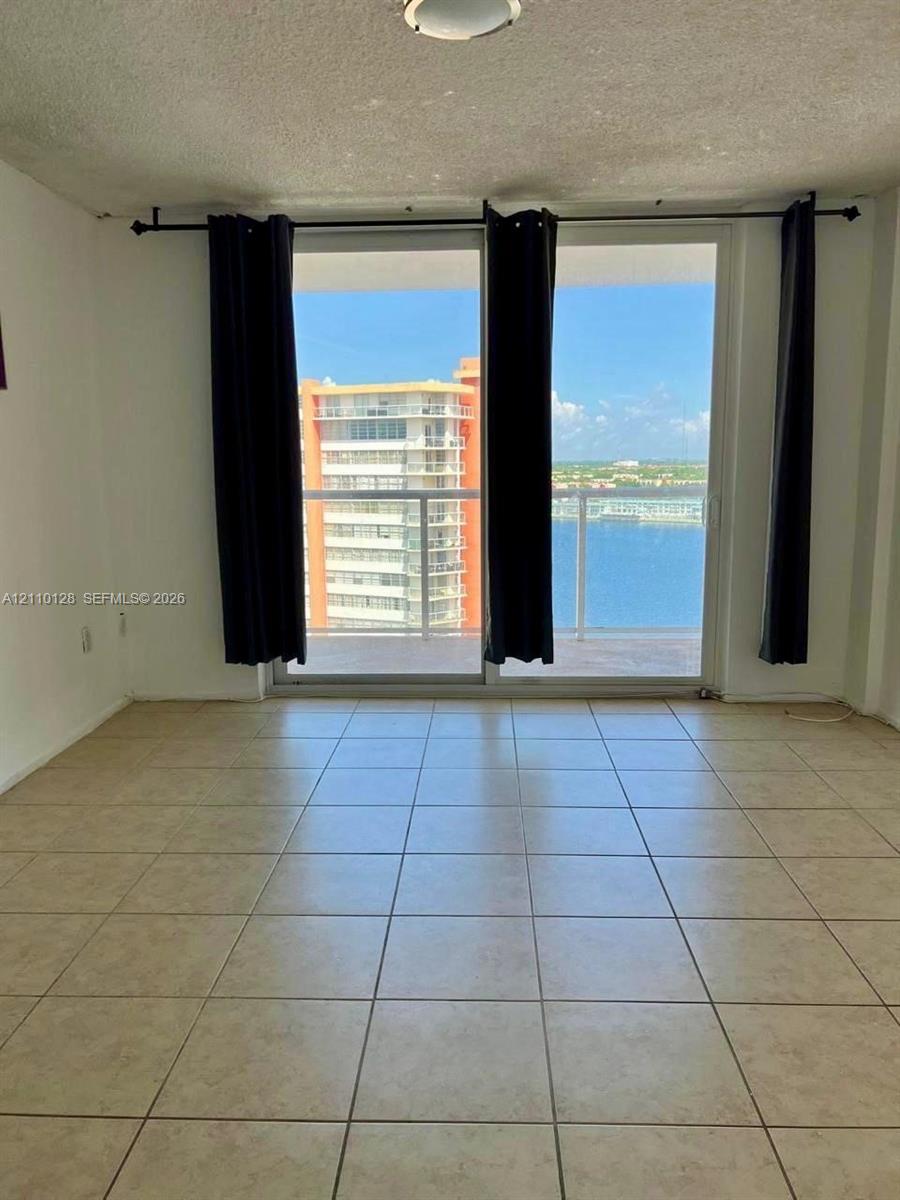Floor-to-ceiling sliding glass doors opening to a balcony with a glass railing and ceramic tile flooring