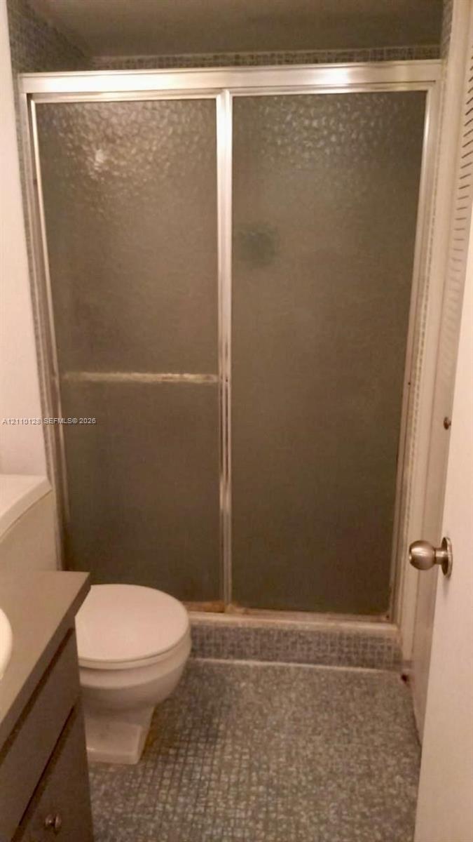 Shower stall featuring a metal-framed enclosure with textured privacy glass and a tiled floor, accompanied by a built-in vanity cabinet and standard porcelain toilet