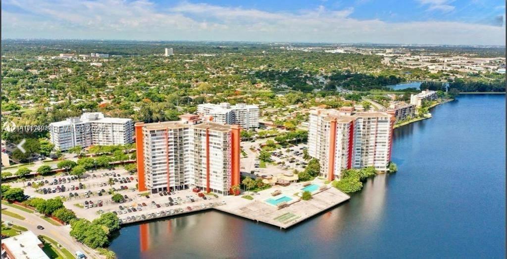 Aerial perspective of a multi-story residential complex featuring waterfront access, paved surface parking, and a swimming pool