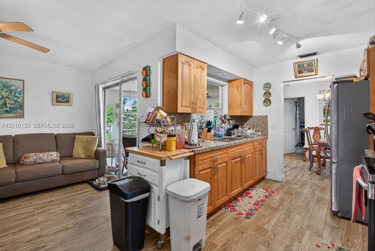 Kitchen featuring wood cabinetry, stone countertops, track lighting, and wood-finish tile flooring with sliding glass door access