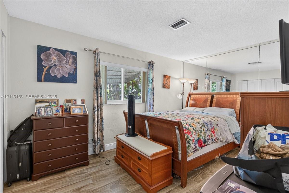 Neutral interior featuring wood-finish flooring, a window with horizontal blinds, and a full-width mirrored wall