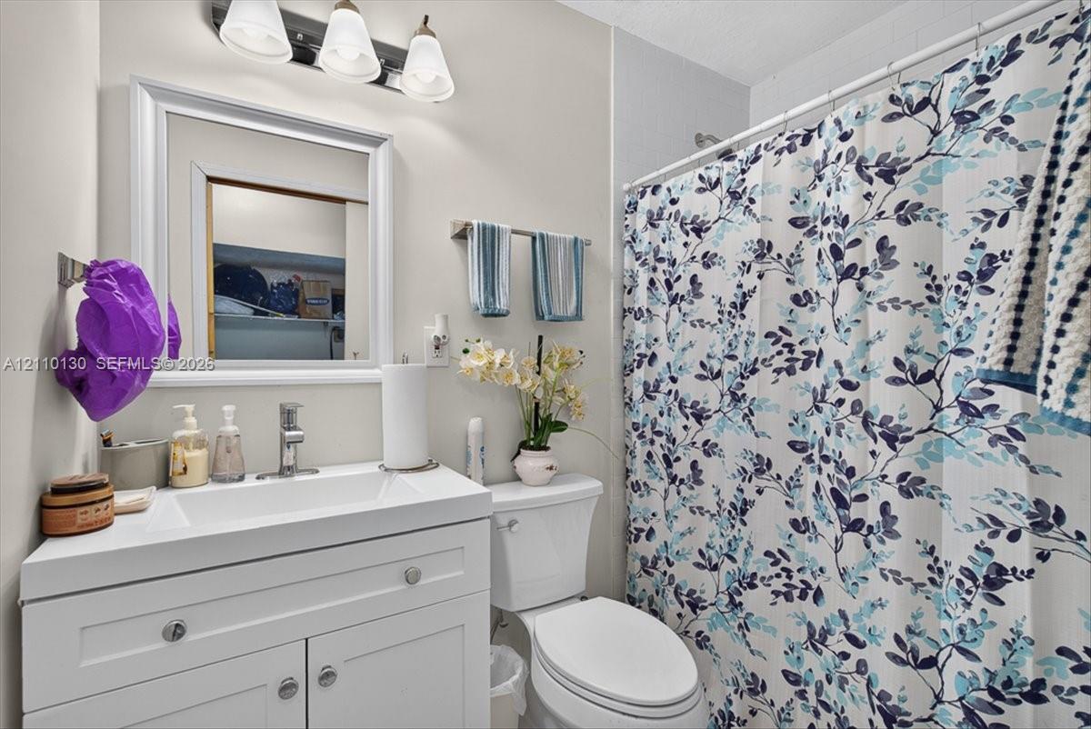 White vanity with integrated rectangular sink, chrome single-handle faucet, framed wall-mounted mirror, three-light overhead fixture, and porcelain toilet