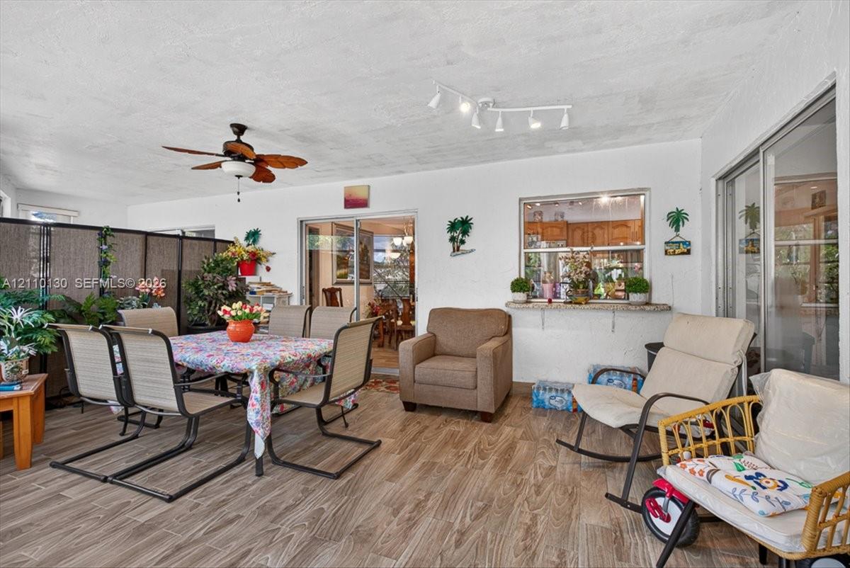 Enclosed patio featuring wood-finish flooring, a ceiling fan, multi-light track lighting, and a passthrough window with a stone-top ledge
