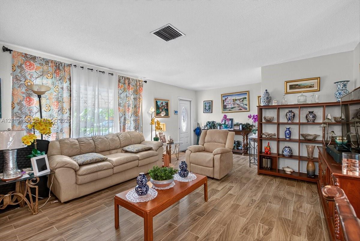 Living area featuring wood-finish tile flooring, neutral wall paint, and a white front entry door with an oval glass insert