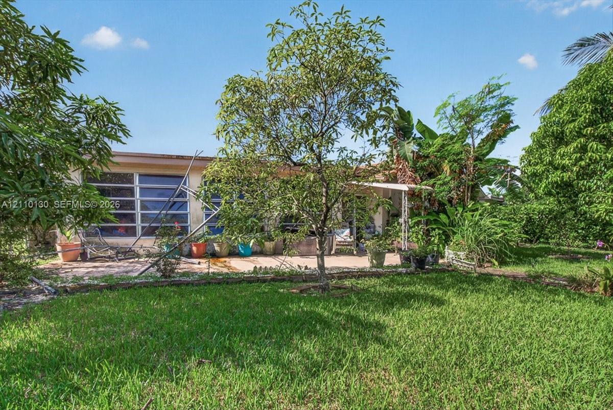 Spacious backyard featuring mature trees, manicured lawn, and a paved patio area with a covered porch