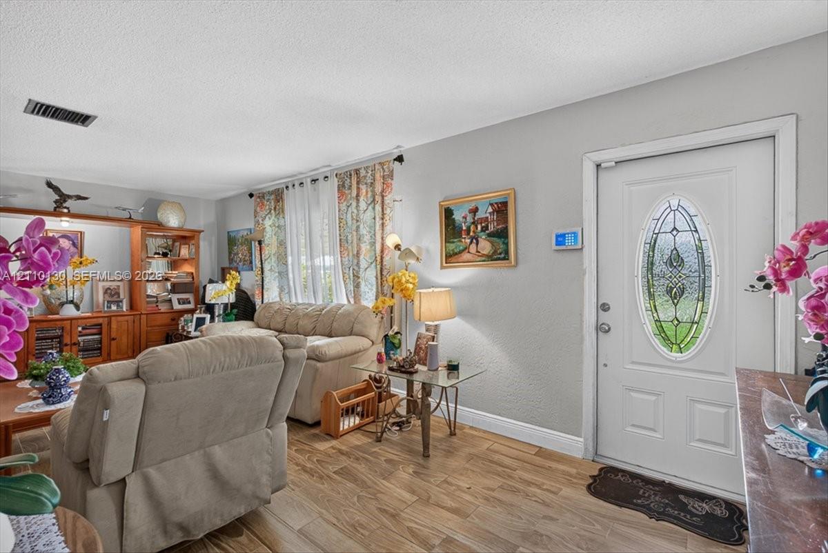 Living area featuring wood-finish flooring, built-in wooden shelving, and a white entry door with an oval decorative glass insert