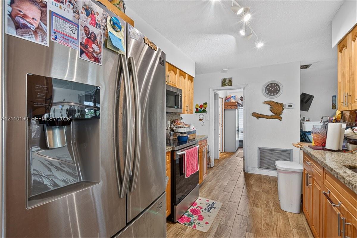 Kitchen featuring wood cabinetry, stone countertops, wood-finish tile flooring, stainless steel appliances, and adjustable track lighting