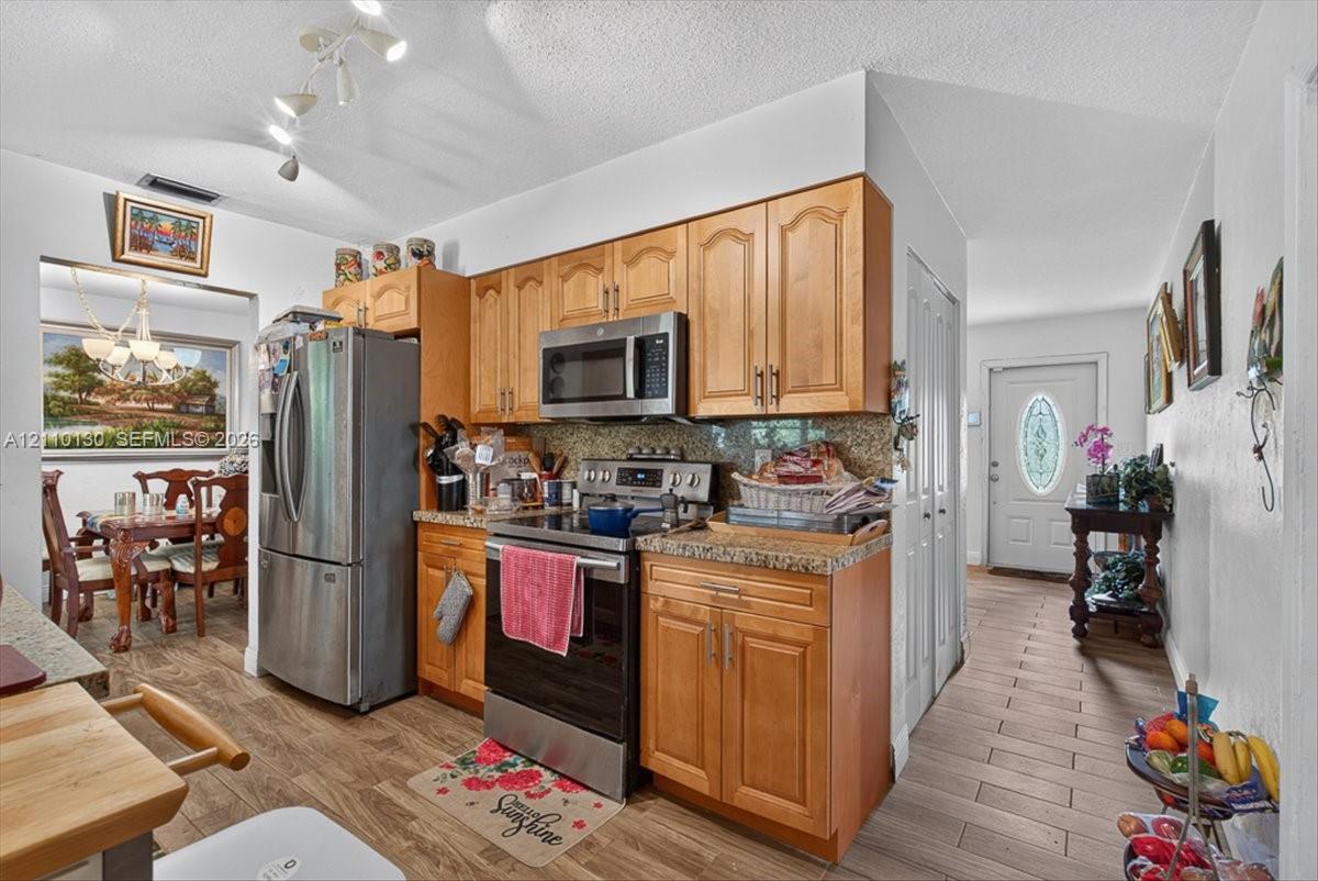 Kitchen featuring wood-finish cabinetry, stone-style countertops, stainless steel appliances, track lighting, and tile flooring